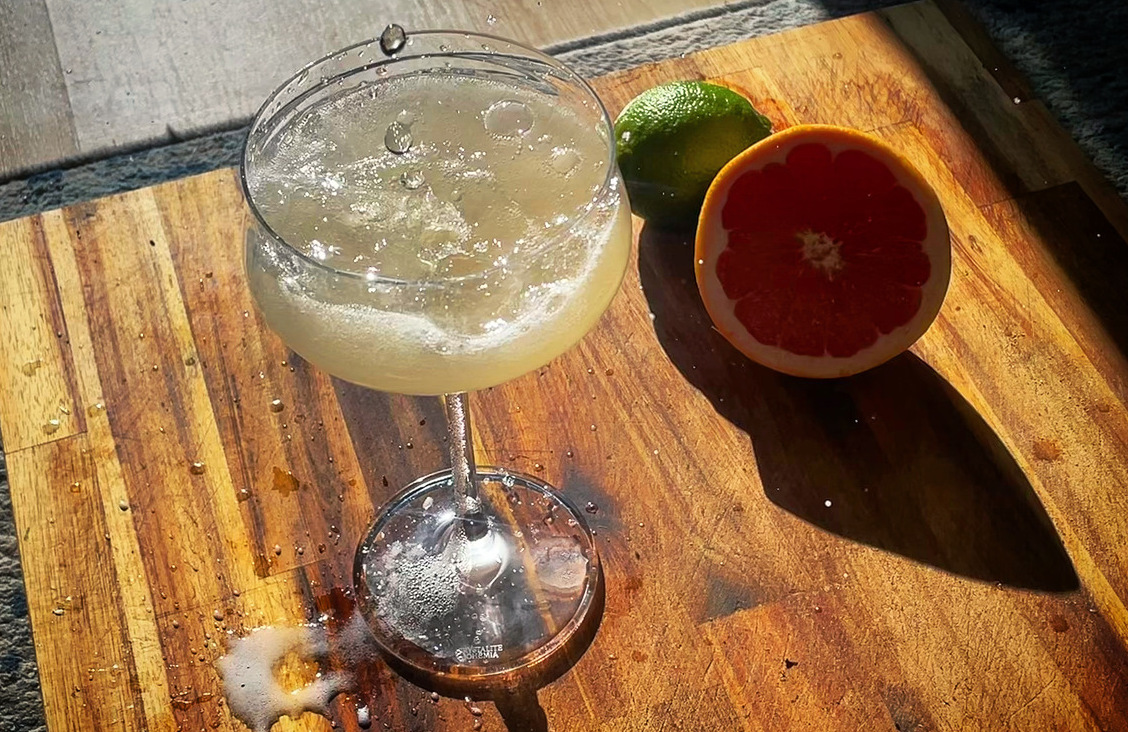 An overhead view of a champagne coup on a wood board in the sunlight, sparkling wine splashing into it